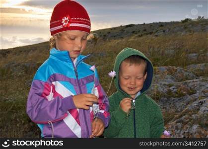 Walking small girl and boy scrutinize prairie flower