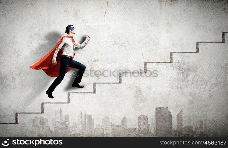 Walking superhero. Young confident superman in mask and cape walking on ladder