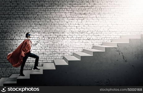 Walking superhero. Young confident superman in mask and cape walking on ladder