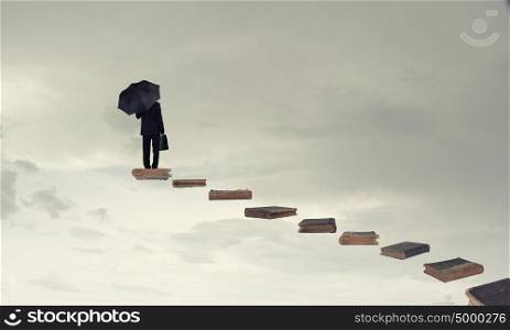 Walking up ladder. Businessman holding umbrella and waking on career ladder made of books
