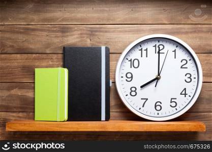 wall clock and book at shelf on wooden background texture