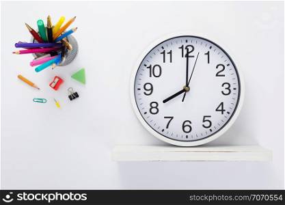 wall clock at wooden shelf and school accessories on white background