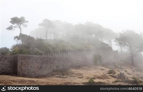 Wall of a fortress on the hillside covered fog