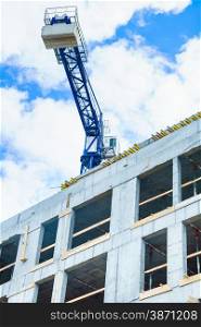 Wall of concrete building and crane on sky background. Construction works. Industrial scene.. Building construction and crane on sky background