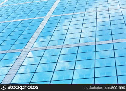 Wall of skyscraper with great number of windows and clouds reflection. Architecture background.