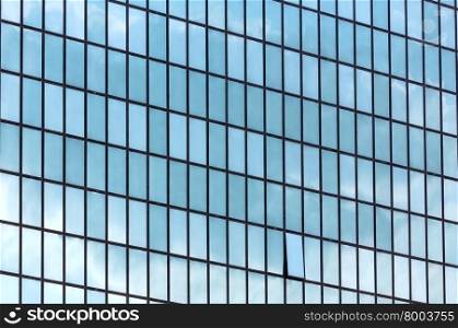 Wall of skyscraper with great number of windows and clouds reflection. Architecture background.