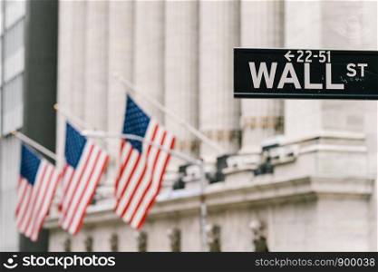 Wall Street sign post with American national flags in background. New York city financial economy district, stock market trade and exchange, or international business concept