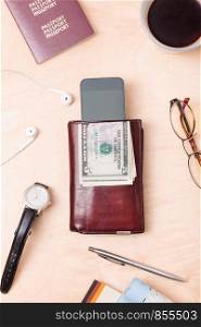 Wallet, dollar banknotes, smartphone, passport, earphones on the wooden desk. Tourist essentials. Things related to travel. Portrait orientation