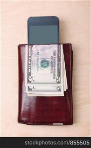 Wallet, smartphone with blank screen and dollar banknotes on wooden table. View from above. Portrait orientation