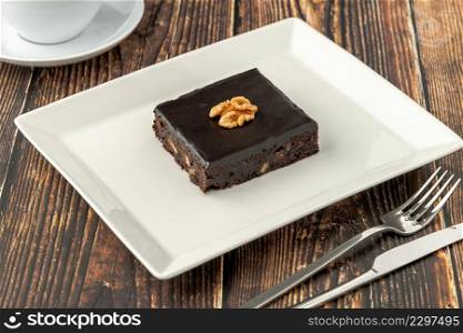 Walnut and dark chocolate brownie on a white porcelain plate on wooden table