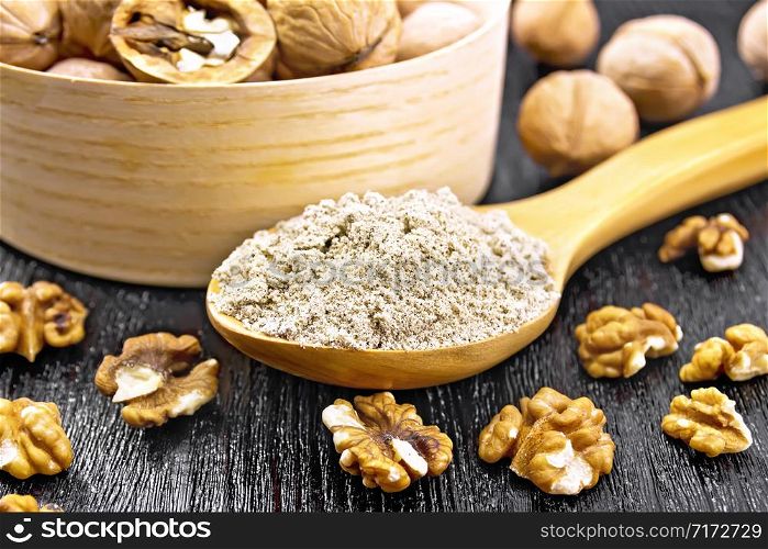 Walnut flour in a spoon, nuts in bowl and on table on background of dark wooden board