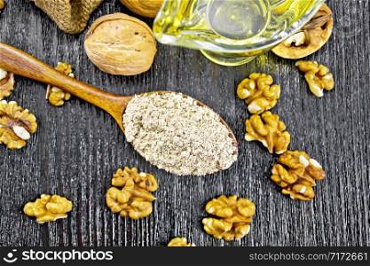 Walnut flour in a spoon, nuts on a table and in bag, oil in a glass sauceboat on wooden board background from above