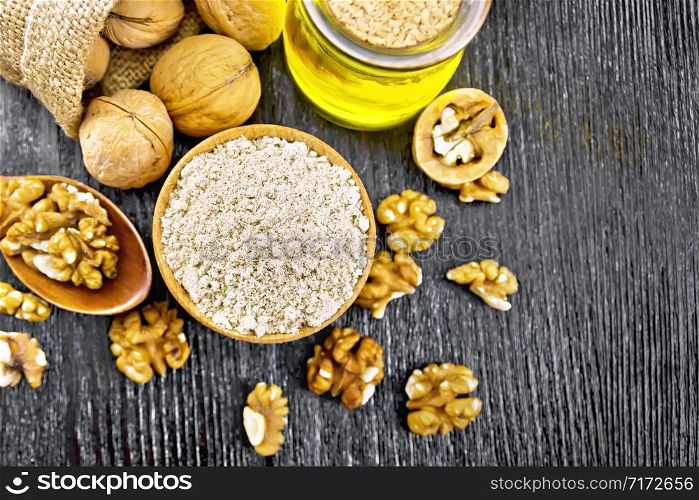 Walnut flour in bowl, nuts on a table, in a spoon and in a bag, oil in glass jar on wooden board background from above