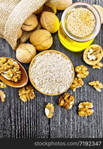 Walnut flour in bowl, nuts on a table, in a spoon and in a bag, oil in glass jar on dark wooden board background from above