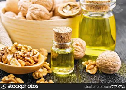 Walnut oil in a glass bottle and a jar, nuts in box, spoon and on the table, burlap napkin on wooden board background