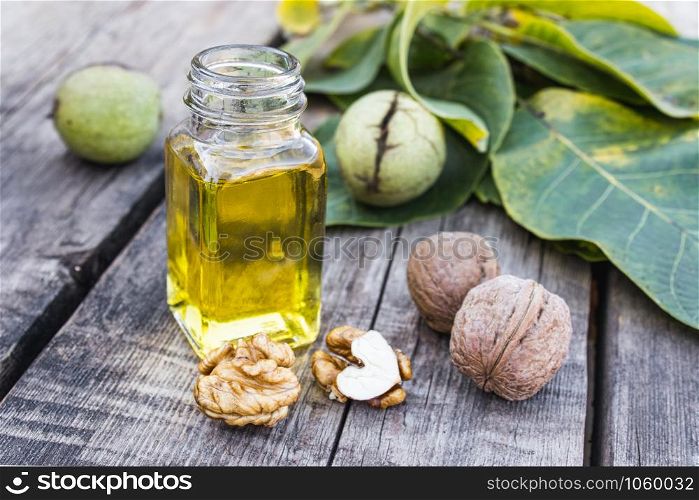 Walnut oil in a glass jar near walnuts and green leaves on a wooden table. Healthy food.. Walnut oil in a glass jar near walnuts and green leaves on a wooden table.