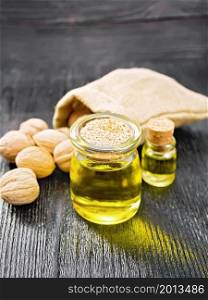 Walnut oil in a jar and a bottle, whole nuts in bag and on table on wooden board background