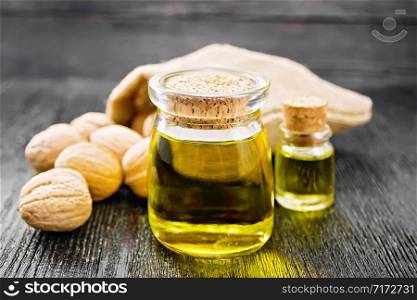 Walnut oil in a jar and a bottle, whole nuts in bag and on table against black wooden board
