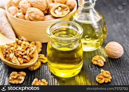 Walnut oil in a jar and decanter, nuts in a box, spoon and on table, burlap napkin on wooden board background