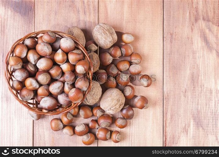 Walnuts and hazelnuts in a basket on wooden background. The view from the top.. Hazelnuts in a basket on a wooden table. The view from the top.