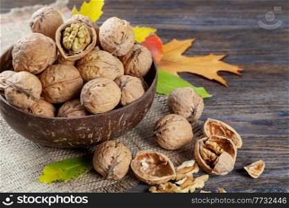 Walnuts on a brown wooden background. Whole nuts in a coconut bowl with autumn maple leaves