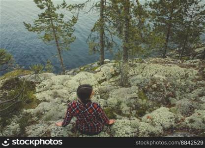Wanderlust scenic photography. Picture of female hiker sitting on mountain cliff with spruce trees, water on background. High quality wallpaper. Photo concept for ads, travel blog, magazine, article. Wanderlust scenic photography