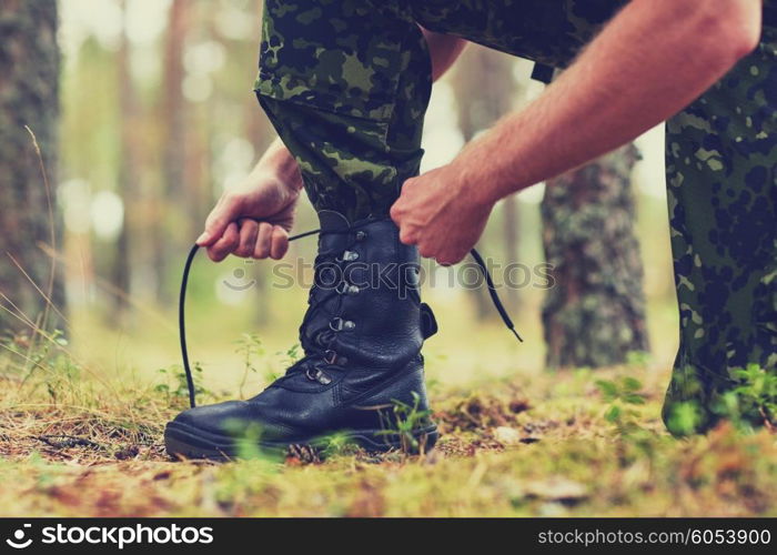 war, hiking, army and people concept - close up of soldier boots and hands tying bootlaces in forest