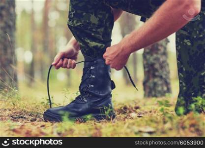 war, hiking, army and people concept - close up of soldier boots and hands tying bootlaces in forest