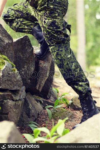war, hiking, army and people concept - close up of soldier legs climbing on rocks in forest