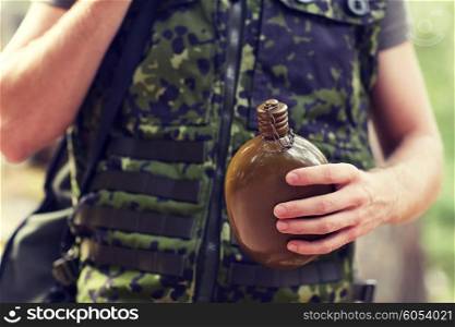 war, hiking, army and people concept - close up of young soldier or ranger with gun drinking from flask in forest