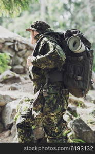 war, hiking, army and people concept - young soldier or ranger with backpack walking in forest