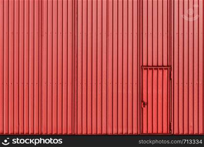 Warehouse facade of coral color, metal sheet wall, and door. Aluminum panel industrial wall and door. The metal door of an industrial building.
