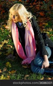 warm and fashion portrait of blond model sitting on the grass in a sunny winter day with hair style