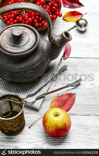 Warm apple berry tea. clay kettle with tea with berries on autumn background