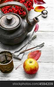 Warm apple berry tea. clay kettle with tea with berries on autumn background