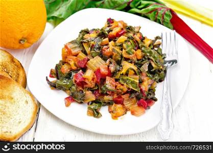 Warm chard salad with orange and onion in a plate, toasted bread, fork on a wooden board background