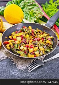 Warm chard salad with orange and onion in an old frying pan on sackcloth, bread, fork on a wooden board background