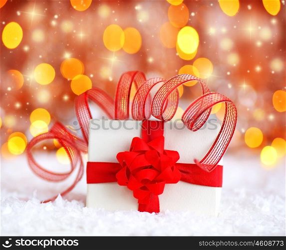 Warm holiday background with white present gift box wrapped with red ribbon &amp; bow, Christmas ornament and new year decoration over defocus lights
