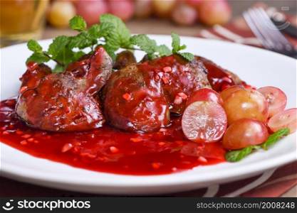 Warm salad with chicken liver and grapes on the plate. Warm salad from turkey liver. Warm salad with chicken liver in raspberry sauce.
