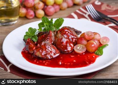 Warm salad with chicken liver and grapes on the plate. Warm salad from turkey liver. Warm salad with chicken liver in raspberry sauce.