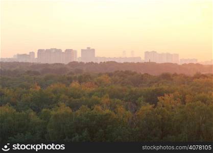 warm summer sunrise over urban houses and park in early morning