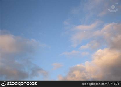 Warm sunset clouds and moon on a blue background.