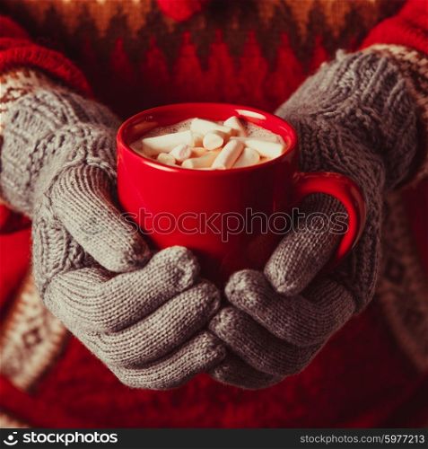 Warm winter photo which hands in knitted gloves holding a mug cocoa with marshmallow. Cocoa with marshmallow