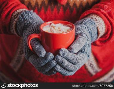 Warm winter photo which hands in knitted gloves holding a mug cocoa with marshmallow. Cocoa with marshmallow