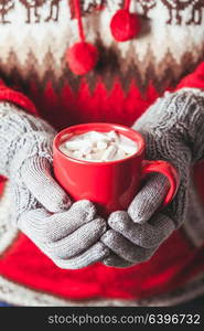 Warm winter photo which hands in knitted gloves holding a mug cocoa with marshmallow. Cocoa with marshmallow