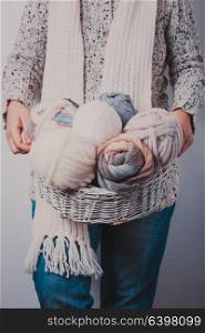 Warmly dressed woman holding a basket of balls of woolen yarn. Woman with basket of balls of woolen yarn