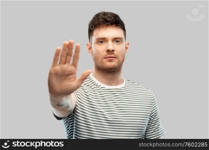 warning and people concept - serious young man in striped t-shirt showing stop gesture over grey background. serious young man showing stop gesture
