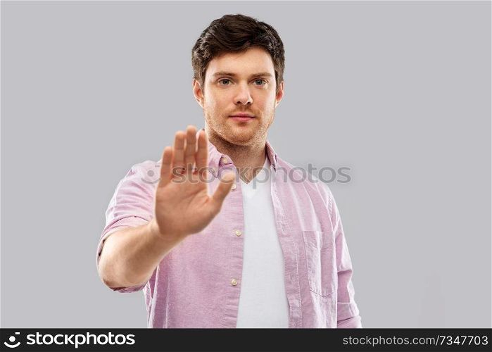 warning and people concept - serious young man showing stop gesture over grey background. serious young man showing stop gesture