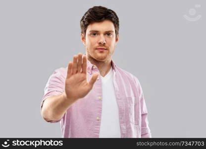 warning and people concept - serious young man showing stop gesture over grey background. serious young man showing stop gesture