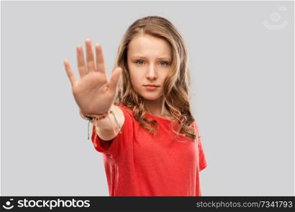warning, prohibition and people concept - serious teenage girl in blank red t-shirt showing stop gesture over grey background. serious teenage girl showing stop gesture